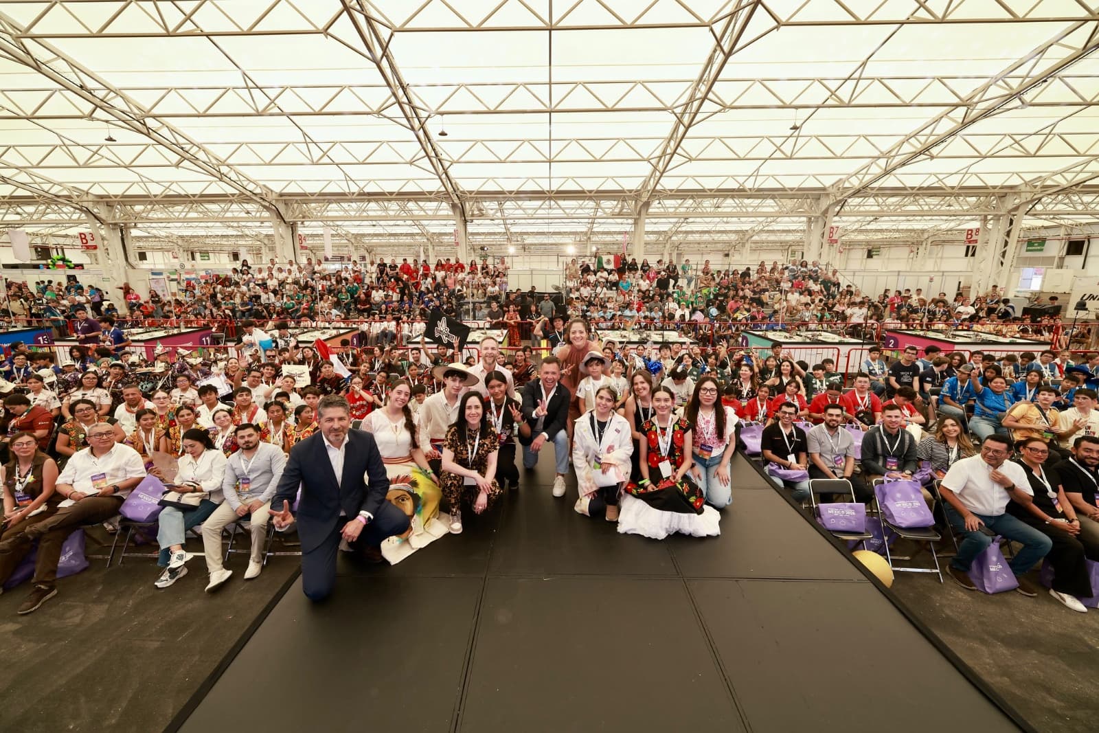 Gran concurrencia de jóvenes en evento cultural, con participantes en vestimenta tradicional y un escenario decorado.