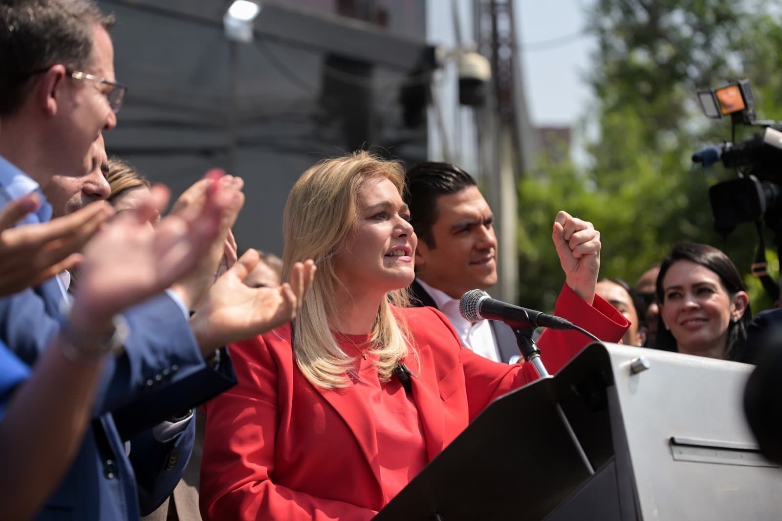 La candidata política pronuncia un discurso en un mitin, rodeada de simpatizantes que aplauden y muestran apoyo.