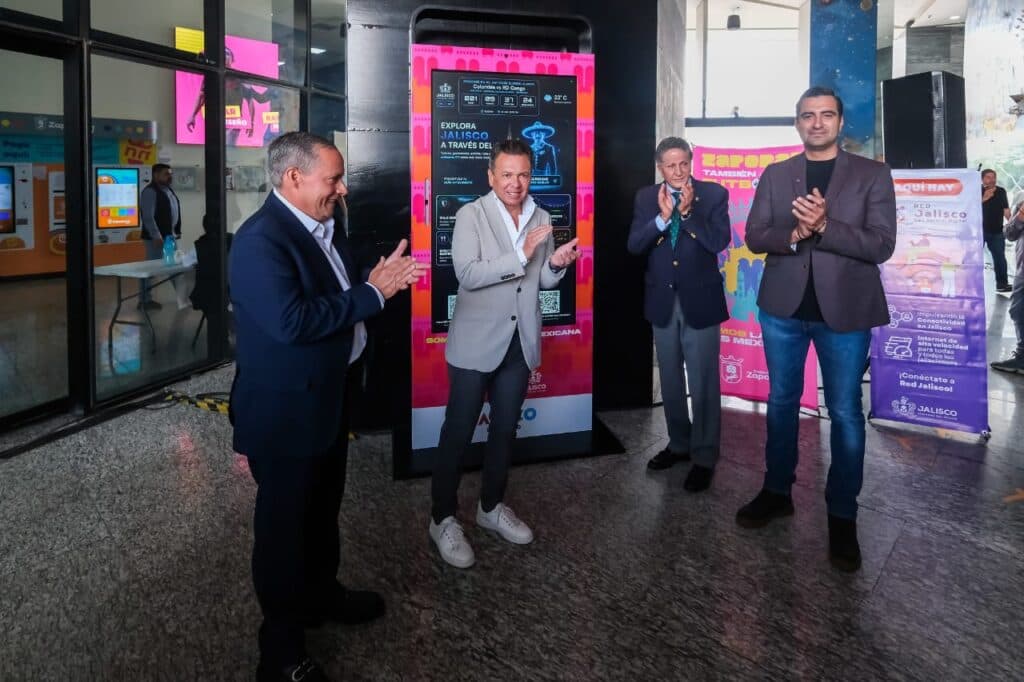 Pablo Lemus Navarro y funcionarios aplauden durante la inauguración de Tótems Inteligentes en Guadalajara, con pantallas informativas al fondo.