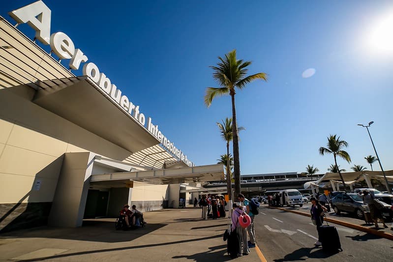 Aeropuerto Internacional de Guadalajara con viajeros y palmeras, escenario del giveaway de vuelos nacionales de Mundo Jalisco.