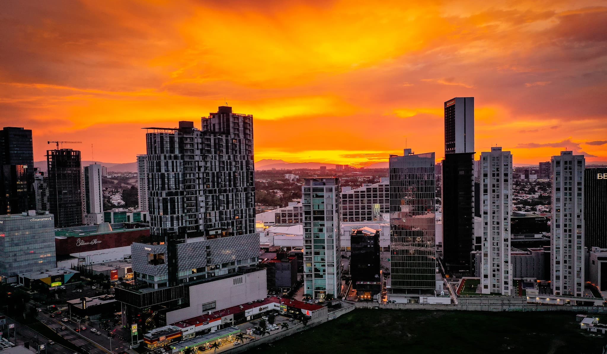 Atardecer sobre el skyline de Guadalajara, Jalisco, con edificios modernos y un cielo anaranjado, reflejando la