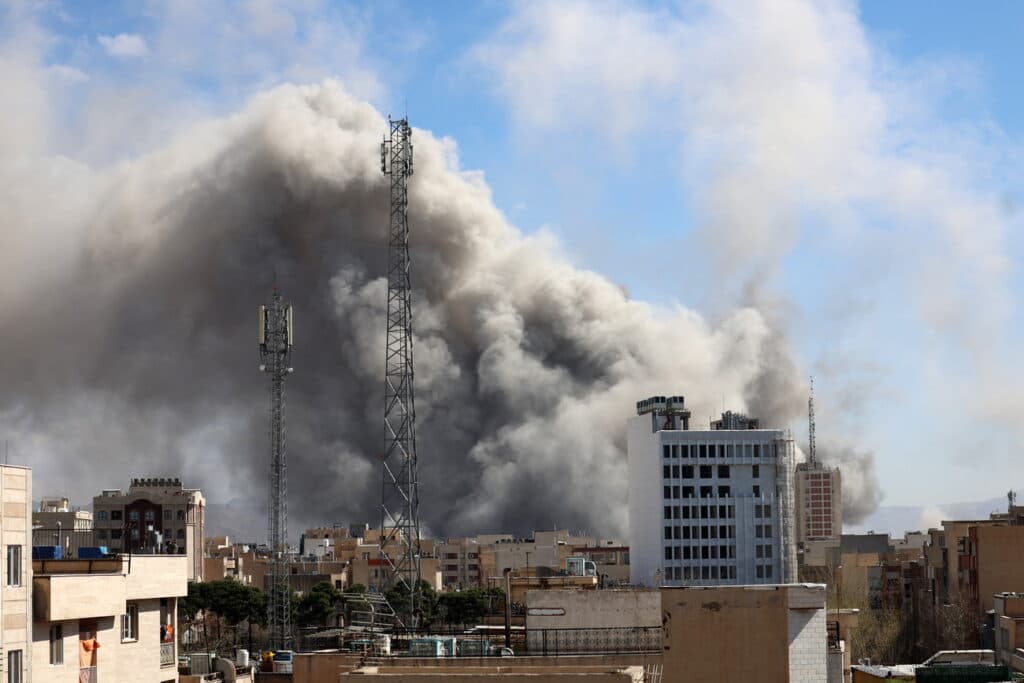 Nubes de humo oscuro se elevan sobre edificios en una ciudad, reflejando la tensión en Medio Oriente tras el anuncio de