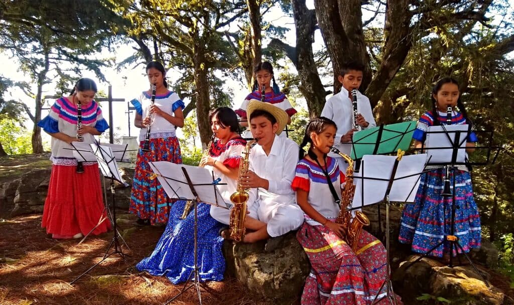 Niños y jóvenes tocando instrumentos musicales en un entorno natural, representando el programa del Sistema Nacional de