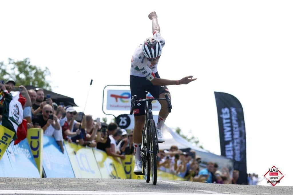 Isaac del Toro celebra su victoria en el Tour Auvergne-Rhône-Alpes 2026, levantando el brazo en señal de triunfo ante una multitud.