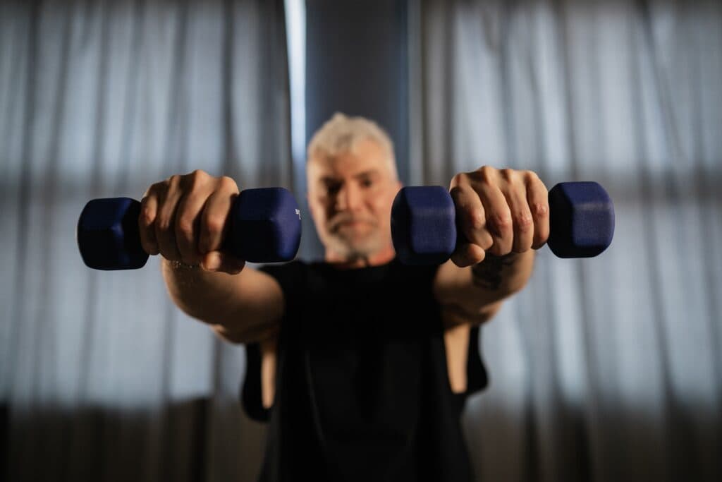 Hombre mayor sosteniendo pesas en un entorno interior, promoviendo el entrenamiento de fuerza para mejorar la calidad de vida.