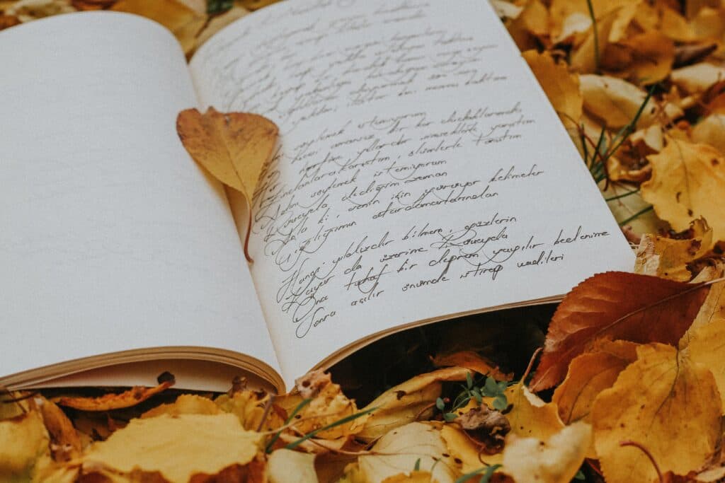Poesía escrita en un cuaderno abierto sobre hojas secas, simbolizando la creatividad literaria en el Premio Nacional de Poesía Jaime Sabines.