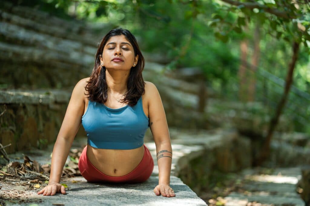 Mujer practicando yoga en un entorno natural, enfocada en la meditación y la respiración, promoviendo la salud mental y física.