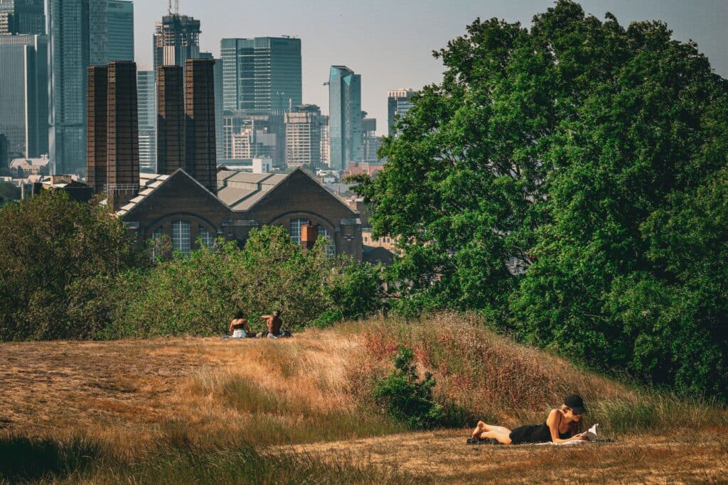 Personas descansando en un área verde de Londres, con edificios modernos al fondo, durante la ola de calor extremo en el Reino Unido.
