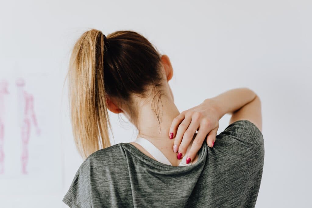 Mujer con cabello recogido se masajea el cuello, evidenciando tensión muscular, reflejando problemas de postura y salud.