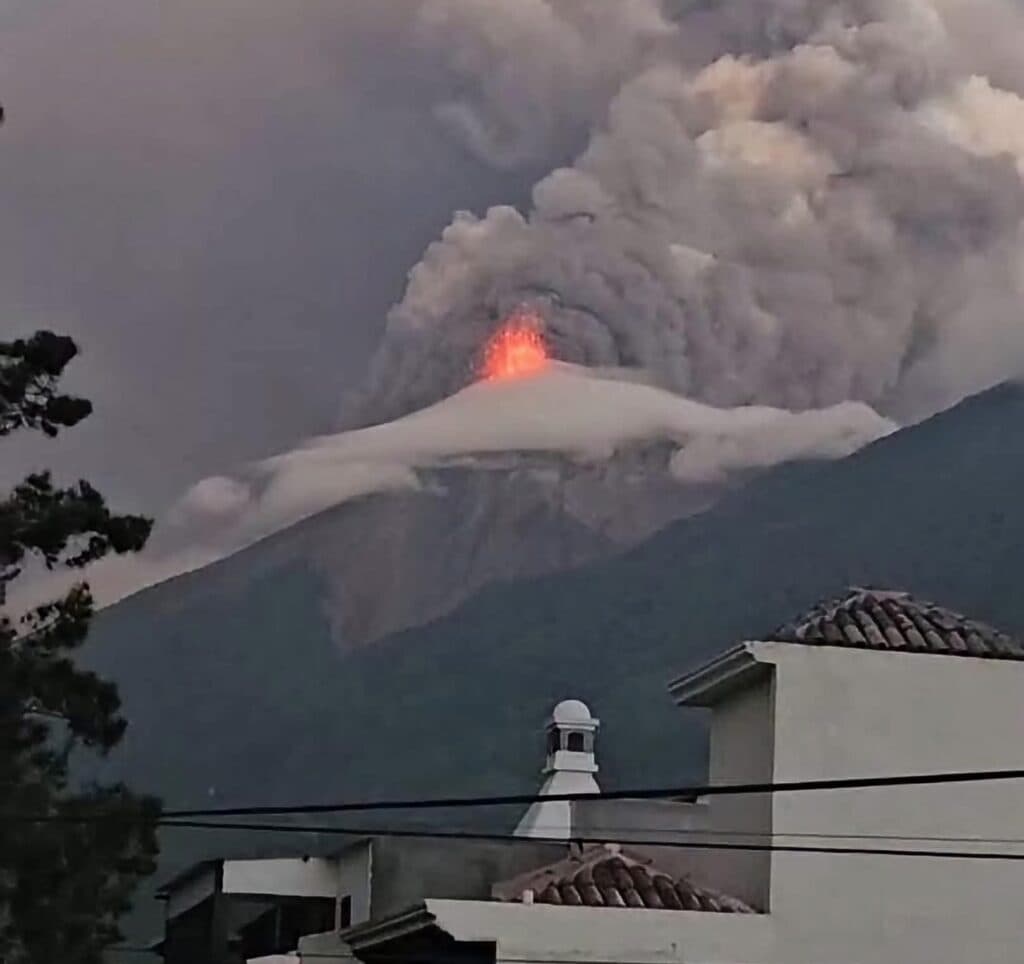 Erupción del Volcán de Fuego en Guatemala, con emisión de lava y ceniza, mientras se observa una nube de gases en el cielo.