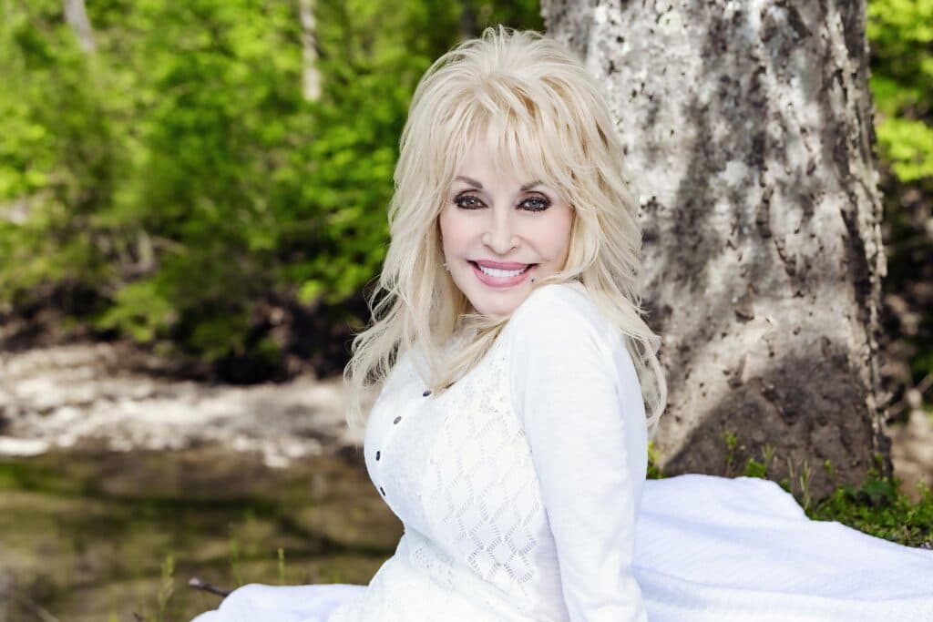 Dolly Parton sonríe en un entorno natural, recordada como una figura icónica de la música country y la filantropía.
