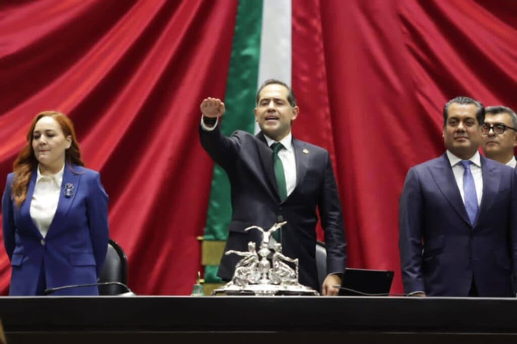 Raúl Bolaños Cacho Cué, nuevo presidente de la Mesa Directiva, levanta la mano en la Cámara de Diputados, con banderas de fondo.