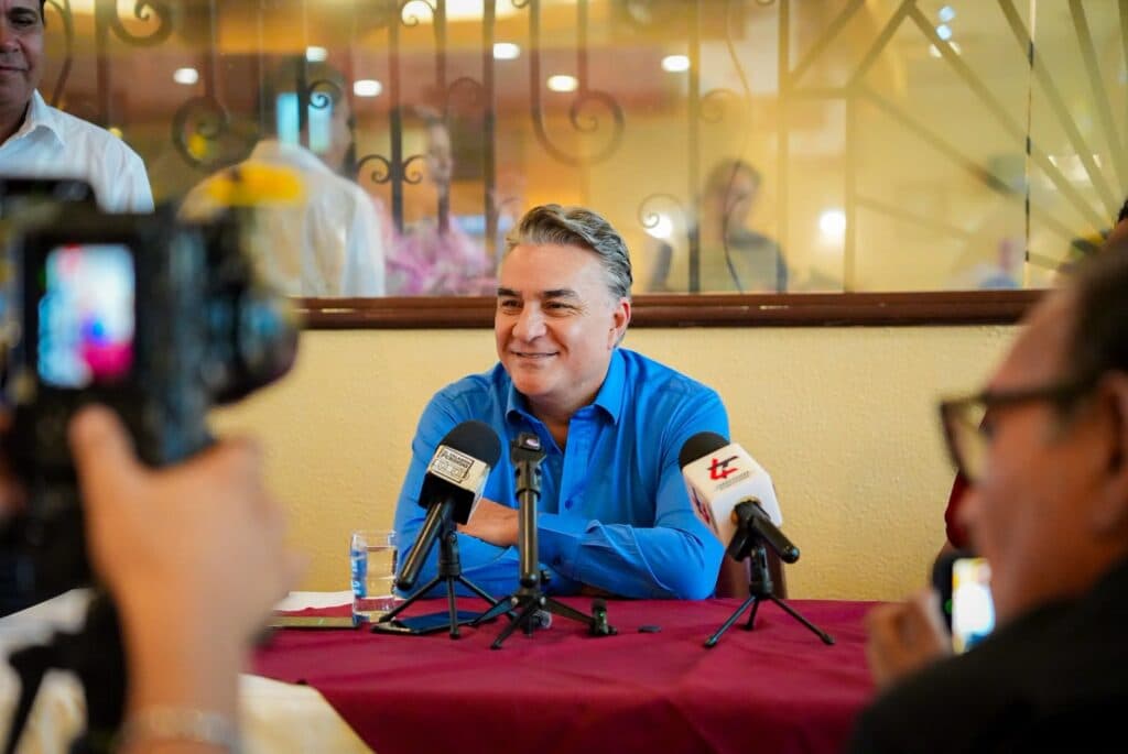 Jesús Ruiz Uribe sonríe durante una conferencia de prensa, rodeado de micrófonos y periodistas, en Mexicali, Baja California.