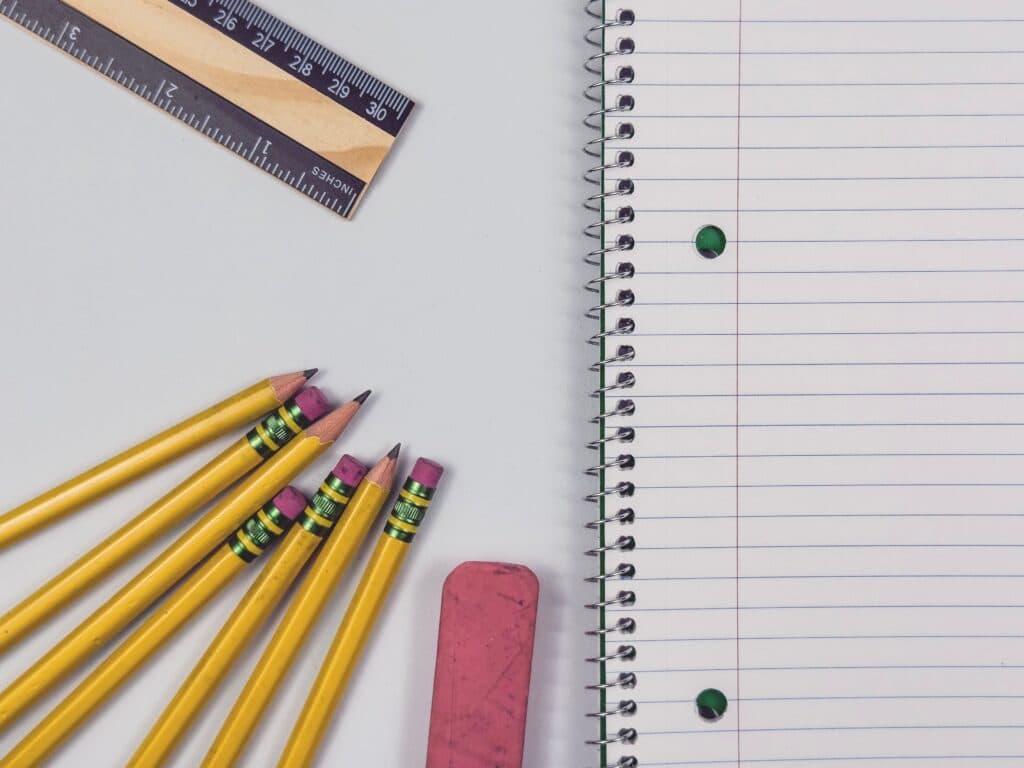 Lápices amarillos, una regla y un cuaderno en blanco sobre una superficie blanca, representando la preparación para el regreso a clases.