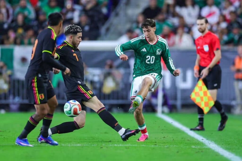 Jugadores de la Selección Mexicana y Perú compiten por el balón durante el partido amistoso, mostrando acción y esfuerzo en el campo.
