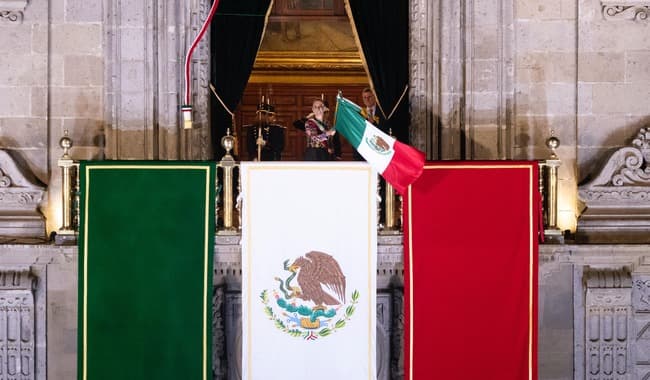 Claudia Sheinbaum en el balcón de Palacio Nacional, ondeando la bandera mexicana durante el Grito de Independencia en el Zócalo.