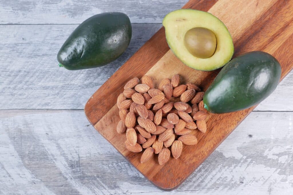 Aguacates y almendras sobre una tabla de madera, alimentos ricos en omega 3 beneficiosos para la salud cardiovascular.